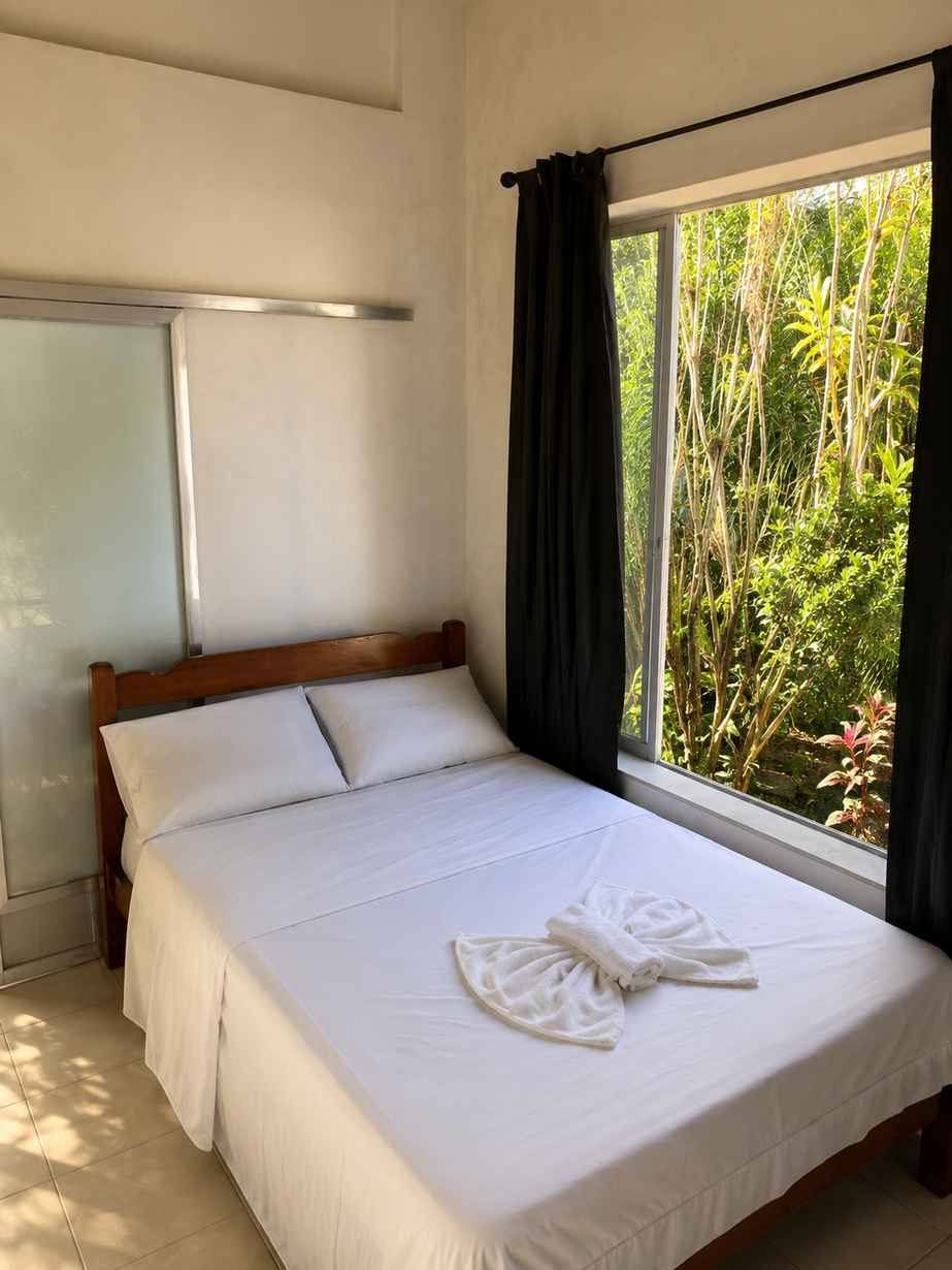 Quarto duplo privativo com vista para o jardim, luminária de vime e plantas tropicais