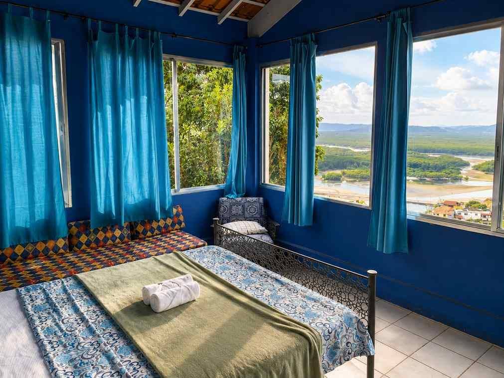 Quarto duplo privativo com janela grande emoldurando o mar e as montanhas verdes no Banana Leaf Eco Hostel